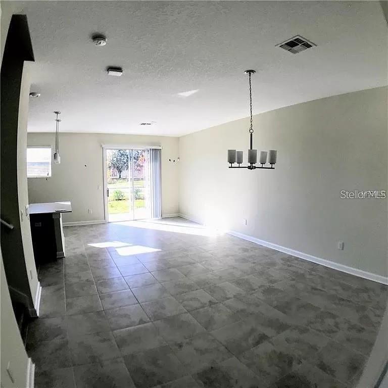 An open-concept dining and living area features gray tile flooring and a modern chandelier — 4652 TRIBUTE TRAIL, KISSIMMEE, FL