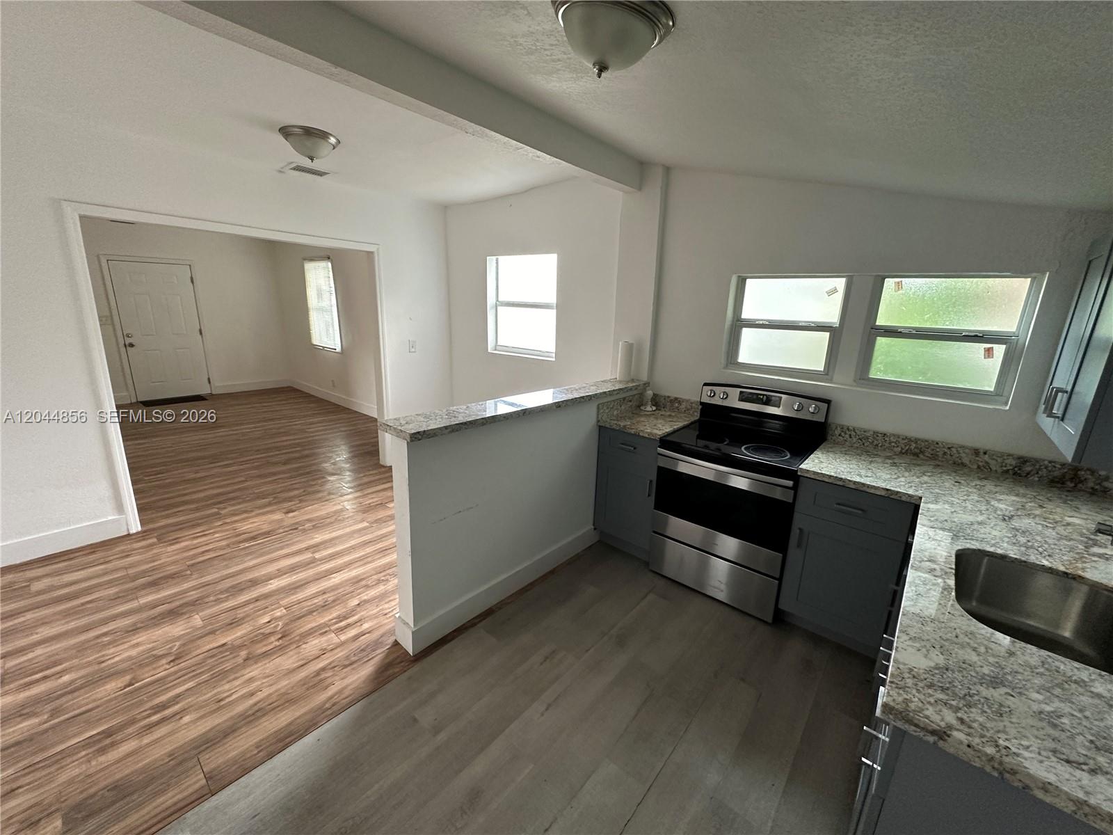 A kitchen with gray cabinets and granite countertops opens into a living area with wood flooring — 5646 NW 3rd Ave # 1, Miami FL 33127, MIAMI, FL