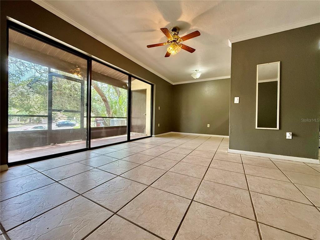 A room with beige tile flooring, dark olive walls, a ceiling fan, and sliding glass doors — 2735 SW 35TH PLACE UNIT 601, GAINESVILLE, FL