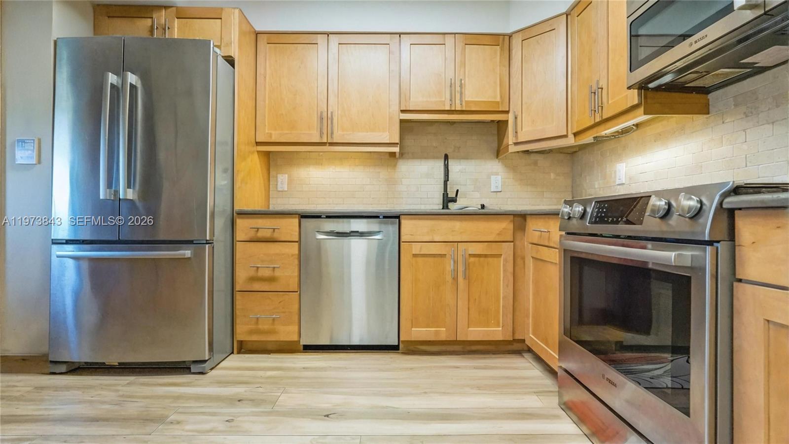 A kitchen features light wood cabinets, stainless steel appliances, and a patterned area rug — 2900 N Course Dr # 804, Pompano Beach FL 33069, POMPANO BEACH, FL