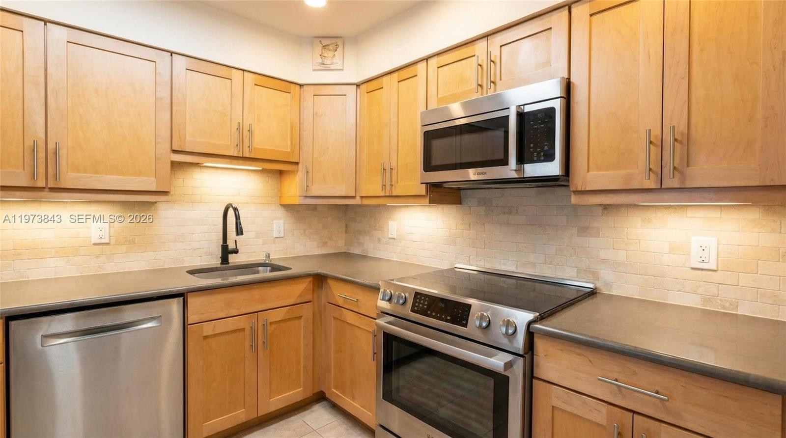 A kitchen features light wood cabinets, stainless steel appliances, and a tiled backsplash — 2900 N Course Dr # 804, Pompano Beach FL 33069, POMPANO BEACH, FL