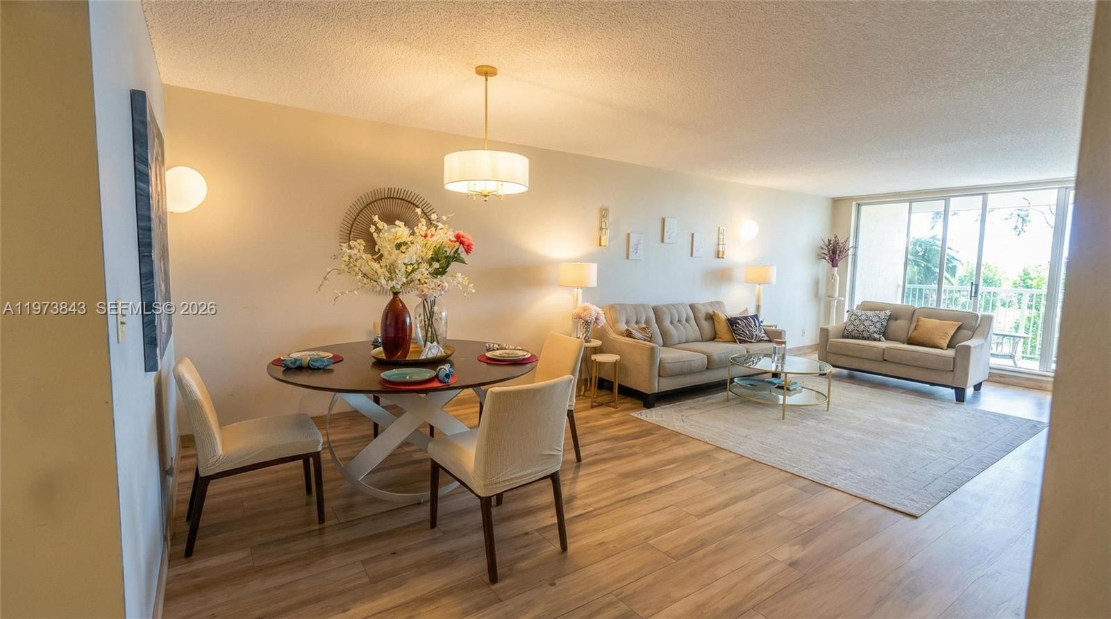 An empty room features light wood-look flooring, a drum pendant light, and sliding glass doors — 2900 N Course Dr # 804, Pompano Beach FL 33069, POMPANO BEACH, FL