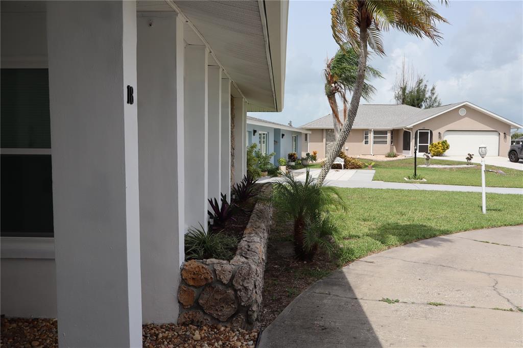 A stone planter box sits along the white exterior wall of a house with palm trees — 18 GOLFVIEW COURT, ROTONDA WEST, FL