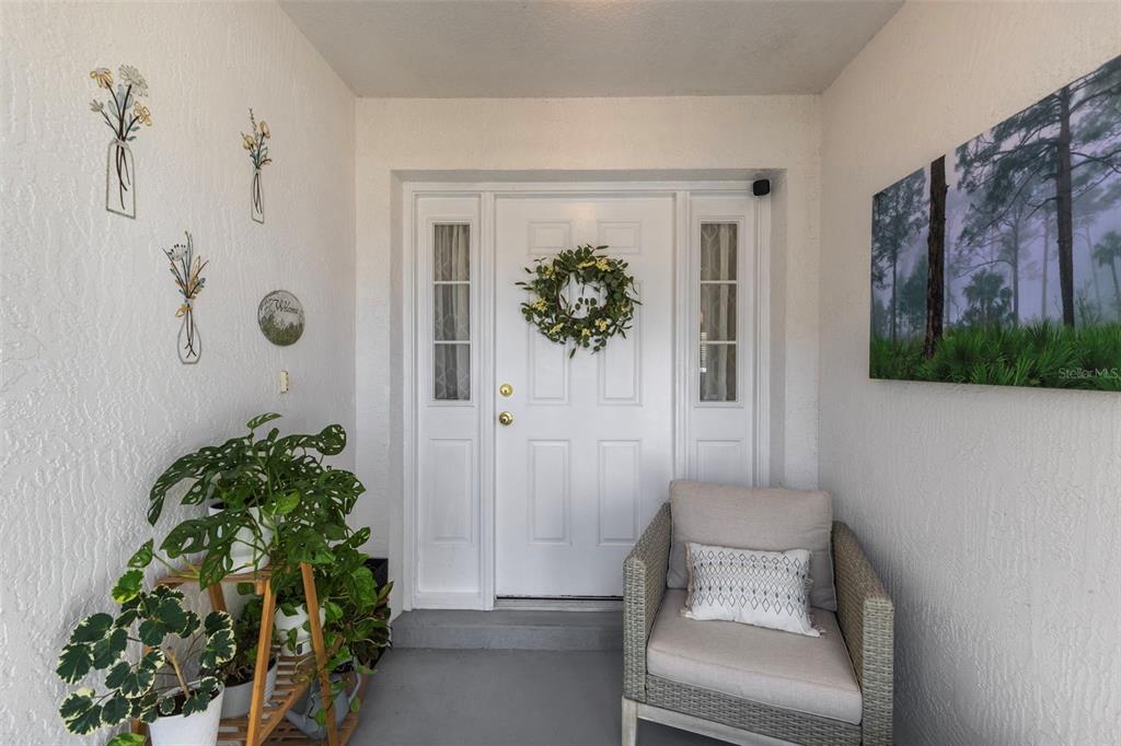 A covered entryway features a white front door, a wicker chair, and potted plants — 11905 LEON AVENUE, PORT CHARLOTTE, FL