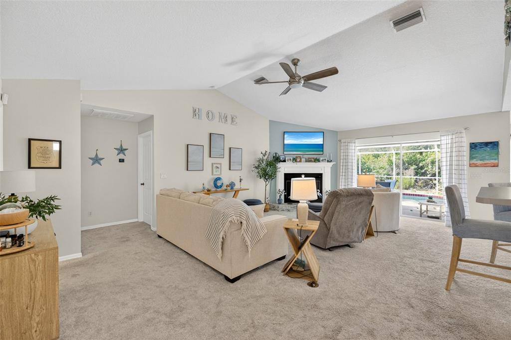 A living room with a beige sofa, fireplace, ceiling fan, and sliding glass doors — 11905 LEON AVENUE, PORT CHARLOTTE, FL