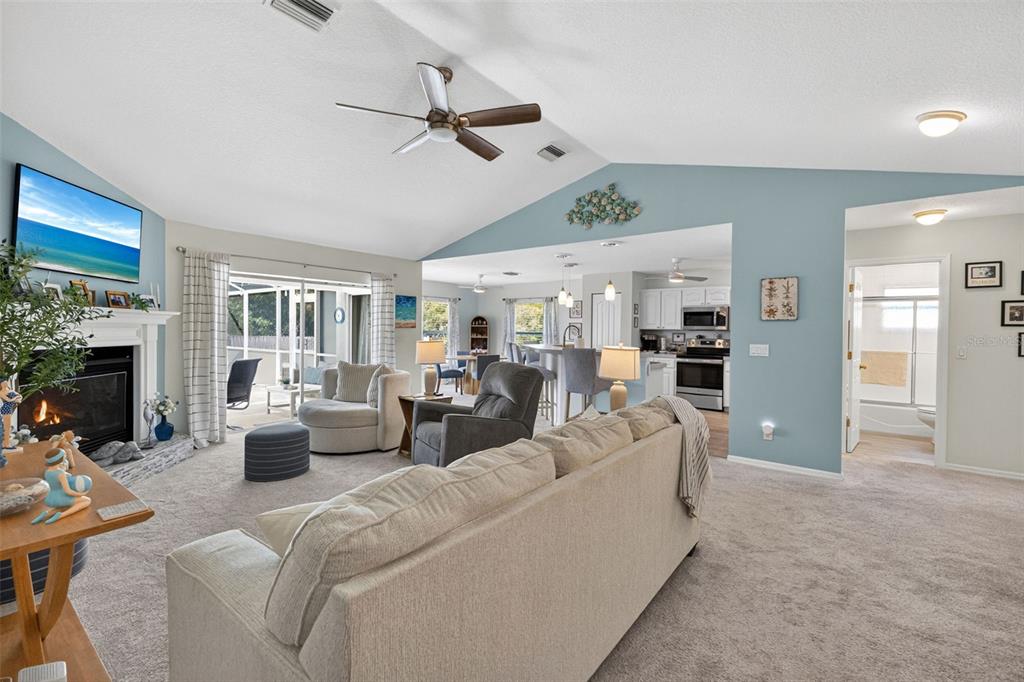A living room with a fireplace, vaulted ceilings, and an open view into the kitchen — 11905 LEON AVENUE, PORT CHARLOTTE, FL