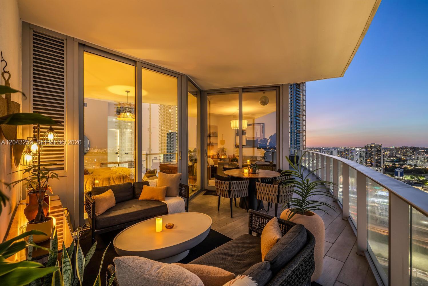 A furnished balcony at dusk features a sofa, coffee table, dining set, and city views — 851 NE 1st Ave # 3403, Miami FL 33132, MIAMI, FL