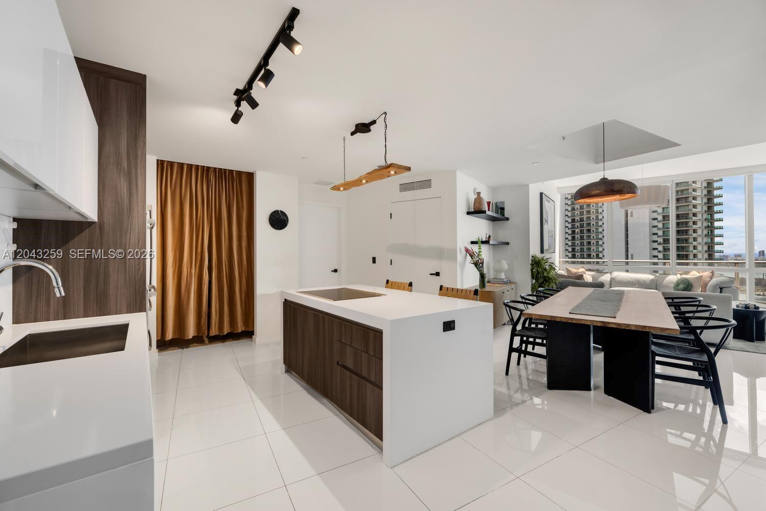 A modern kitchen features a white island, wood cabinetry, and an adjacent dining area — 851 NE 1st Ave # 3403, Miami FL 33132, MIAMI, FL
