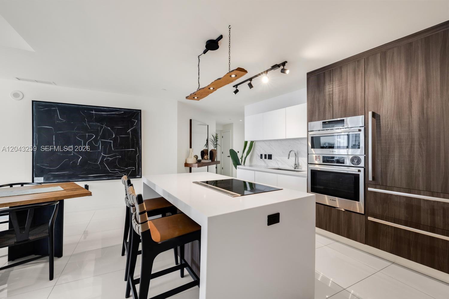 A modern kitchen features a white island with a cooktop, dark wood cabinetry, and track lighting — 851 NE 1st Ave # 3403, Miami FL 33132, MIAMI, FL
