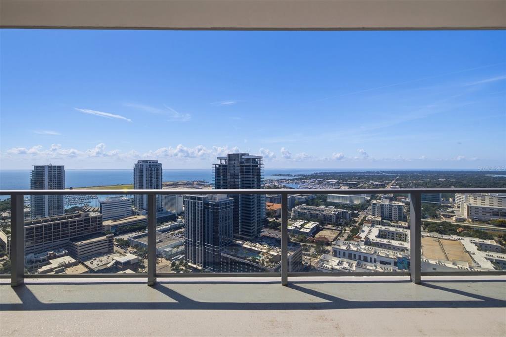 A high-rise balcony overlooks a city skyline, a marina, and the ocean under a blue sky — 400 CENTRAL AVENUE UNIT 3103, ST PETERSBURG, FL
