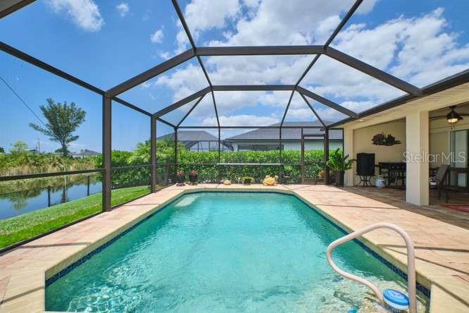 A screened-in swimming pool sits on a patio overlooking a canal and green landscape — 844 NE 6TH AVENUE, CAPE CORAL, FL