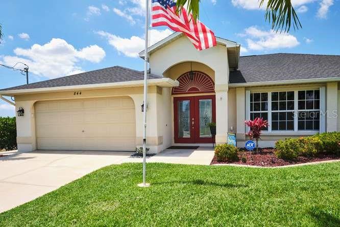 A single-story house with a tan exterior, a two-car garage, and an American flag — 844 NE 6TH AVENUE, CAPE CORAL, FL