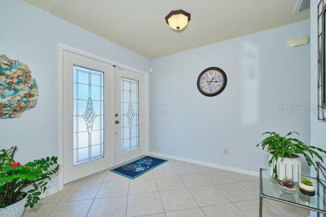 A bright entryway features a double front door with glass inserts, tile flooring, and a clock — 844 NE 6TH AVENUE, CAPE CORAL, FL