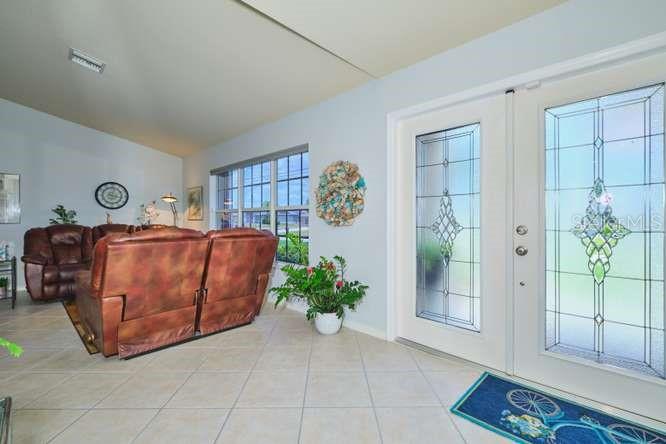A living room with tile floors, a brown leather sofa, and a glass-paneled double door — 844 NE 6TH AVENUE, CAPE CORAL, FL