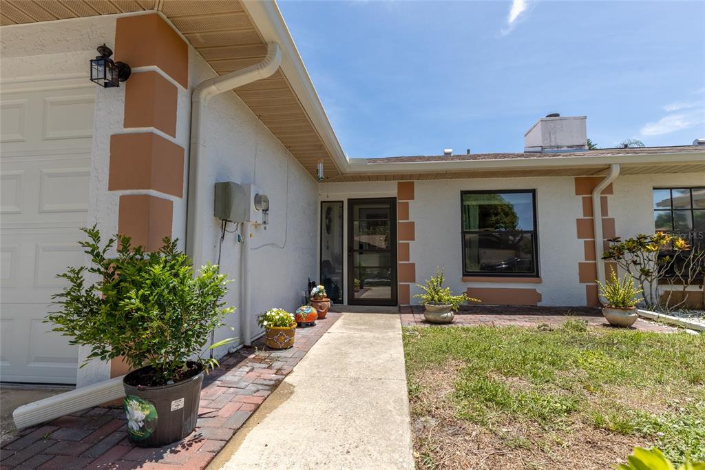 A concrete walkway leads to the front entrance of a house with white stucco walls — 2013 DOVER COURT, OLDSMAR, FL