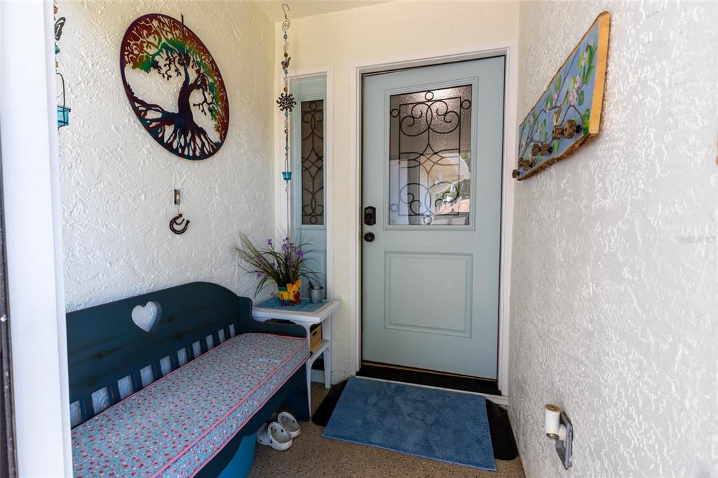 A covered entryway features a light blue front door, a wooden bench, and wall decorations — 2013 DOVER COURT, OLDSMAR, FL