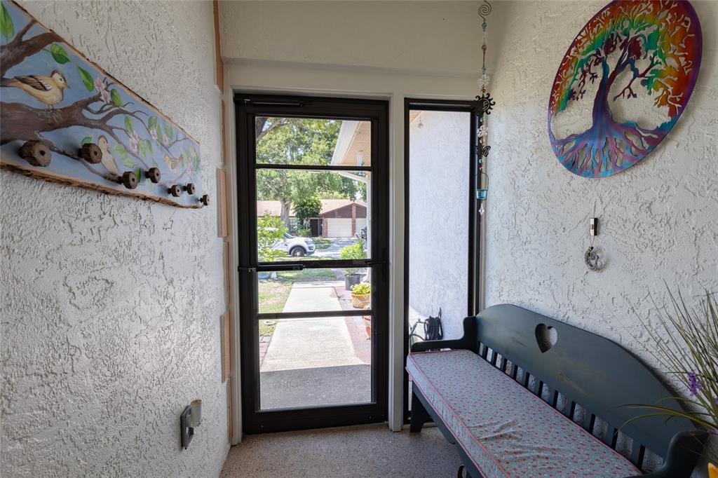 A covered entryway features a screen door, a wooden bench, and wall-mounted decorative art — 2013 DOVER COURT, OLDSMAR, FL