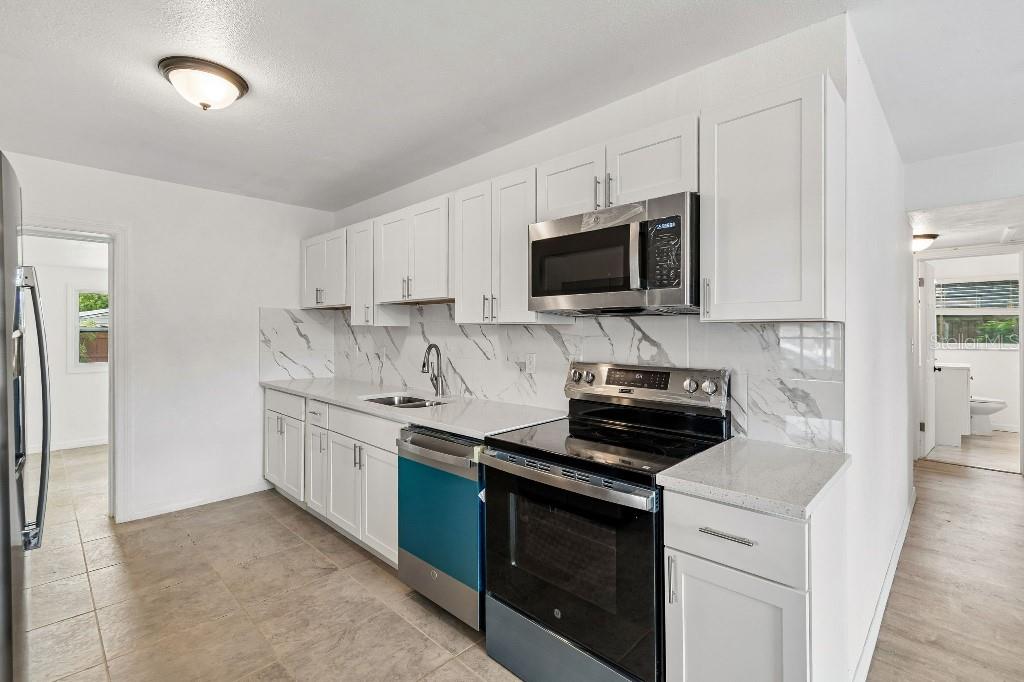 A kitchen with white cabinets, stainless steel appliances, and a marble-patterned backsplash — 203 PEVETTY DRIVE, PLANT CITY, FL