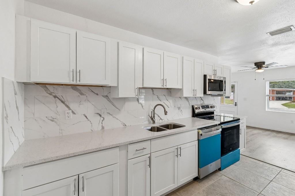 A kitchen with white cabinets, marble-patterned backsplash, light countertops, and stainless steel appliances — 203 PEVETTY DRIVE, PLANT CITY, FL