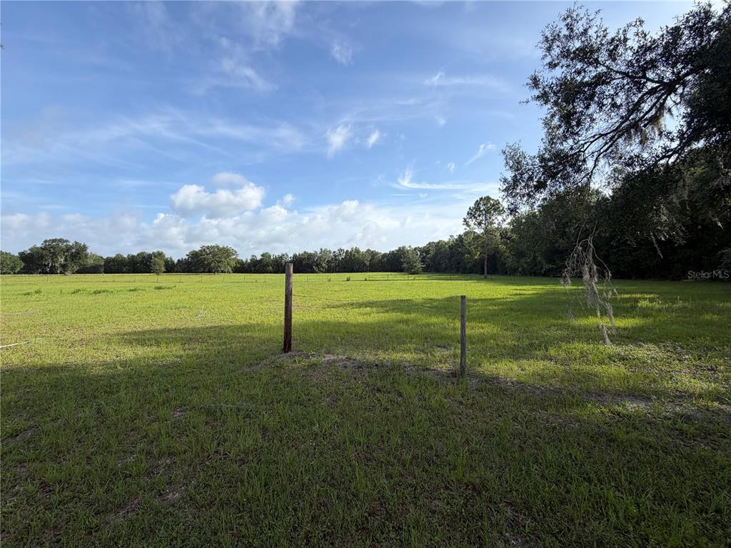 A large, grassy field is enclosed by a wire fence under a partly cloudy sky — PARCEL "B" CR 543, SUMTERVILLE, FL