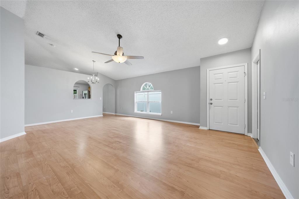 An empty living room features light wood flooring, gray walls, a ceiling fan, and a window — 10617 OPUS DRIVE, RIVERVIEW, FL
