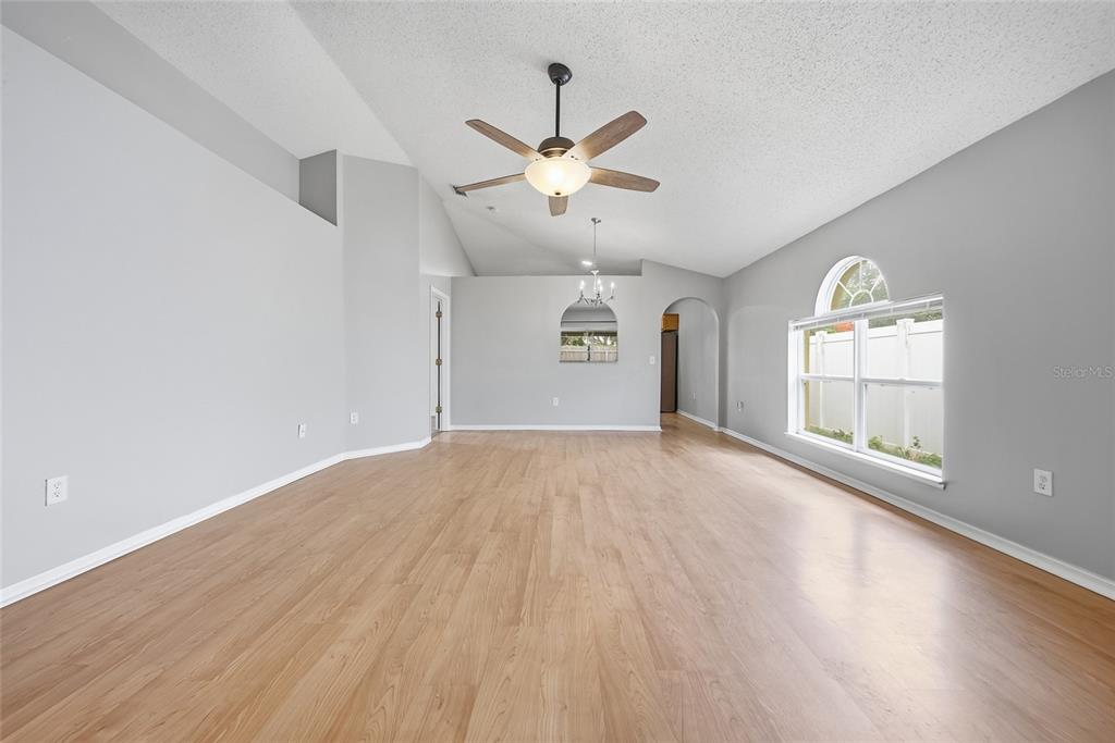An empty living room features light wood-look flooring, gray walls, and a vaulted ceiling — 10617 OPUS DRIVE, RIVERVIEW, FL