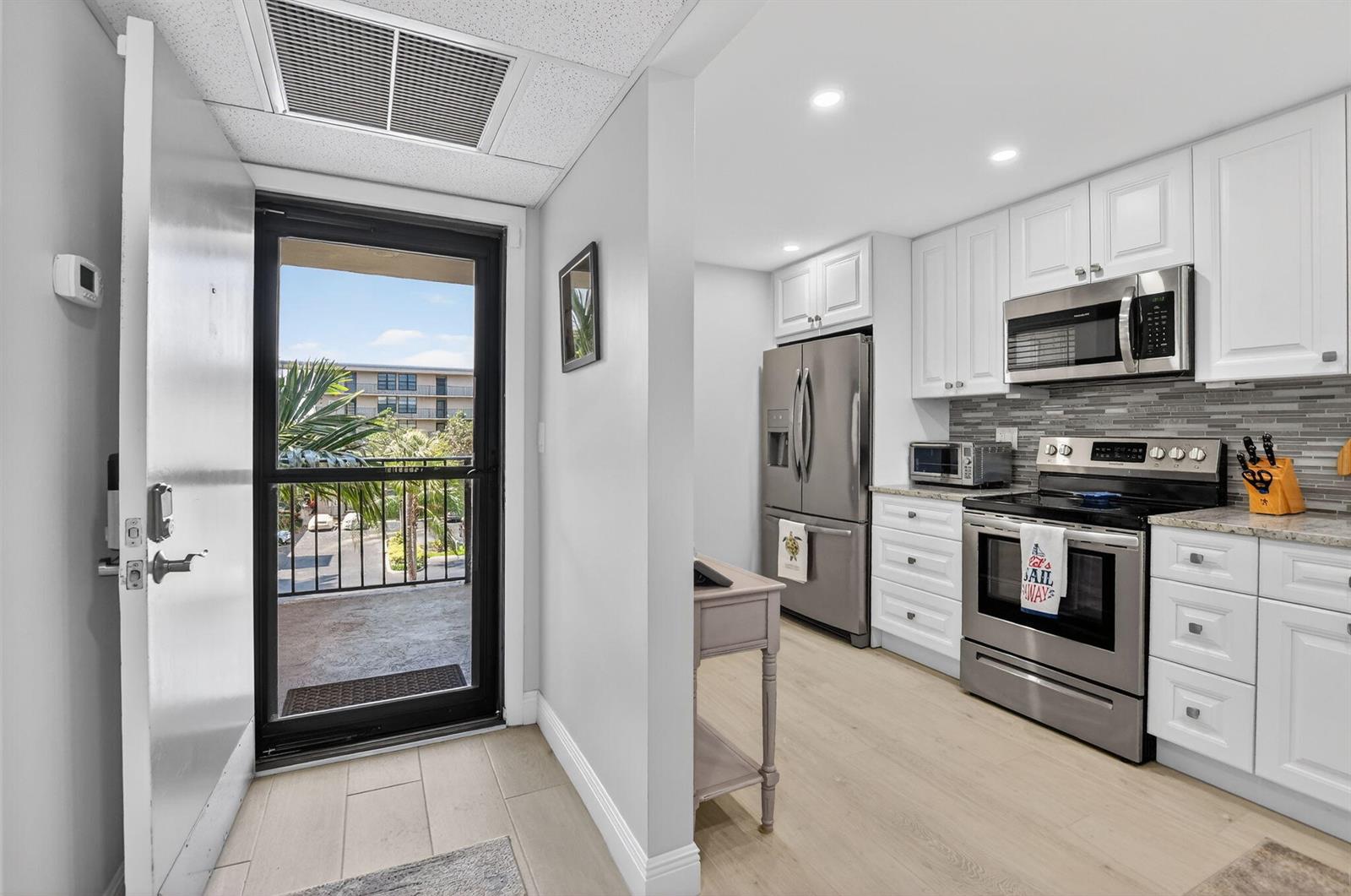 A kitchen with white cabinets and stainless steel appliances opens to a balcony with palm trees — 6 Royal Palm Way # 409, Boca Raton FL 33432, BOCA RATON, FL