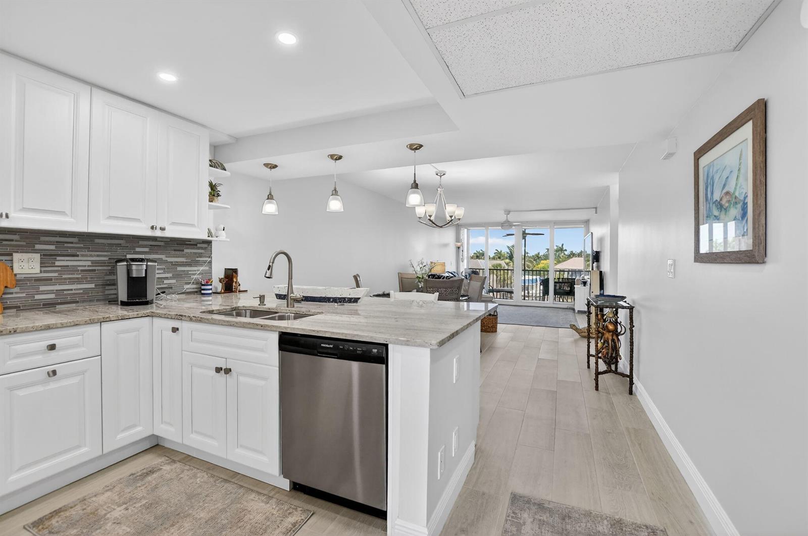 A kitchen with white cabinets and granite countertops opens into a living area with balcony access — 6 Royal Palm Way # 409, Boca Raton FL 33432, BOCA RATON, FL