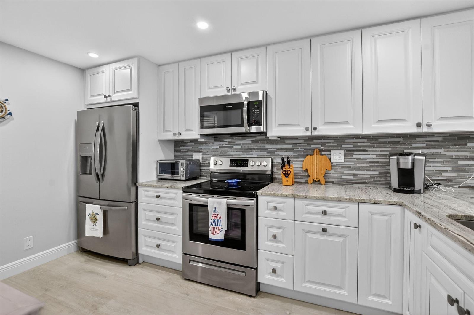 A kitchen features white cabinets, stainless steel appliances, granite countertops, and a gray tile backsplash — 6 Royal Palm Way # 409, Boca Raton FL 33432, BOCA RATON, FL