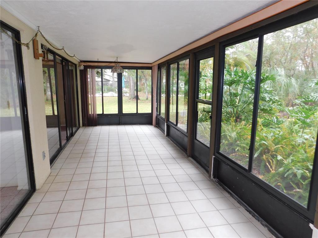 A sunroom with white tiled floors, large glass windows, and a view of outdoor greenery — 60 WOODS LANDING TRAIL, OLDSMAR, FL