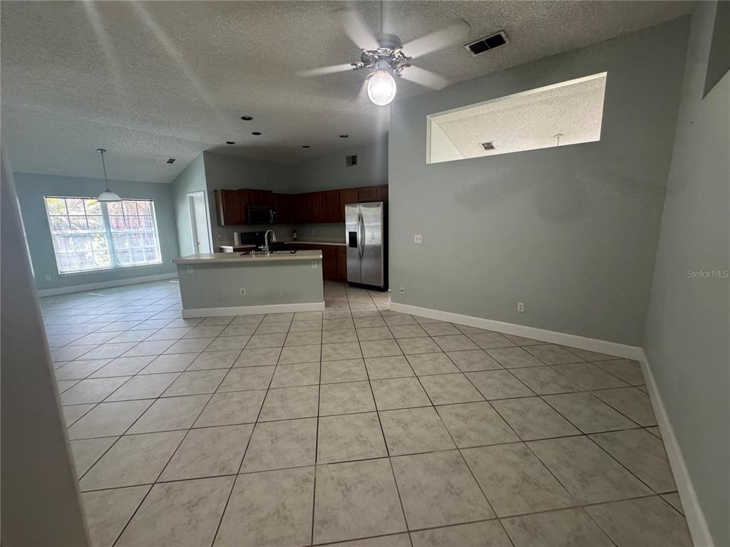 A kitchen with wood cabinets and a stainless steel refrigerator opens to a tiled dining area — 10941 MILL POND WAY, ORLANDO, FL