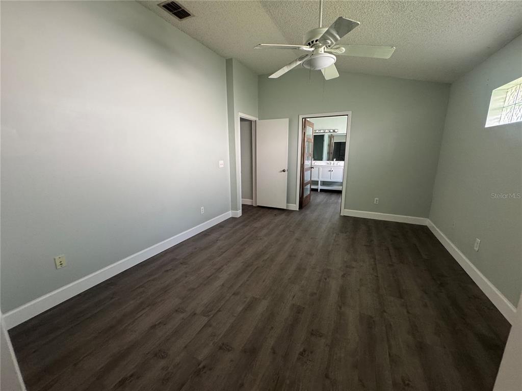 An empty bedroom features light green walls, dark wood-look flooring, and an attached bathroom — 10941 MILL POND WAY, ORLANDO, FL