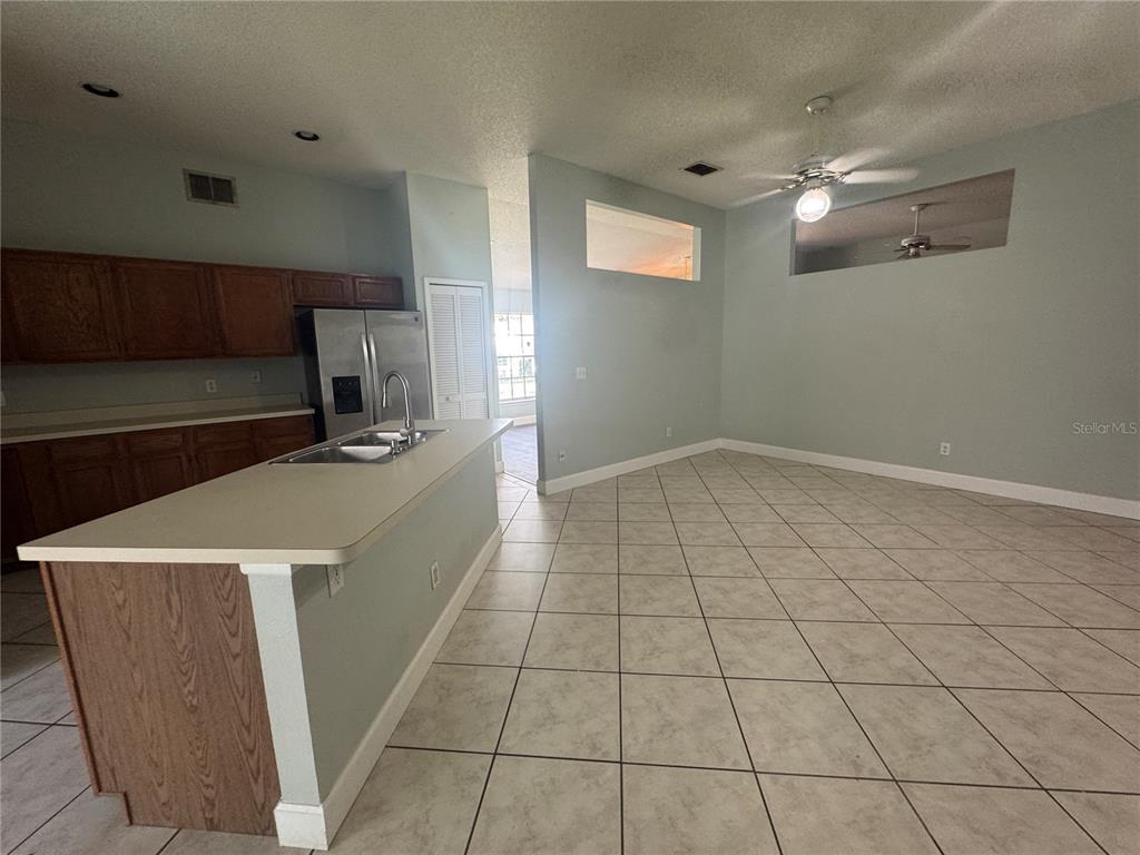 A kitchen with wood cabinets and a breakfast bar opens into a tiled living area — 10941 MILL POND WAY, ORLANDO, FL