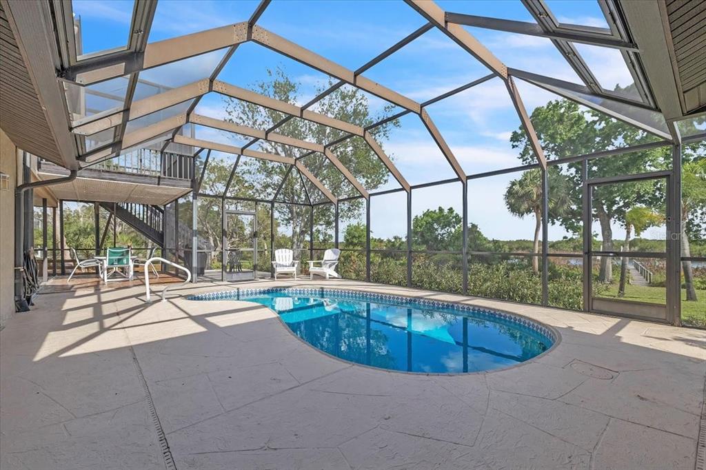 A screened-in pool enclosure features a kidney-shaped pool, concrete deck, and views of trees — 3264 PARK DRIVE, PUNTA GORDA, FL