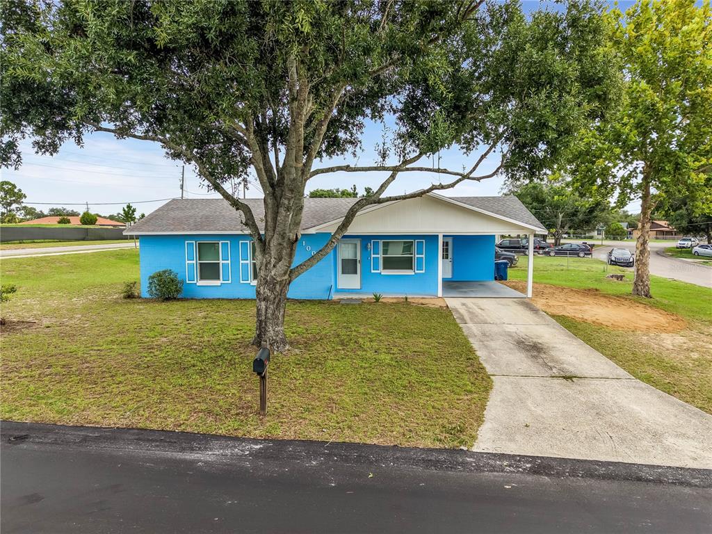 A bright blue single-story house with a carport and a large tree in the yard — 1000 VALENCIA AVENUE, HAINES CITY, FL