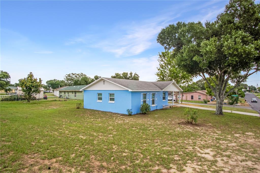 A bright blue single-story house sits on a large grassy lot with a large tree — 1000 VALENCIA AVENUE, HAINES CITY, FL