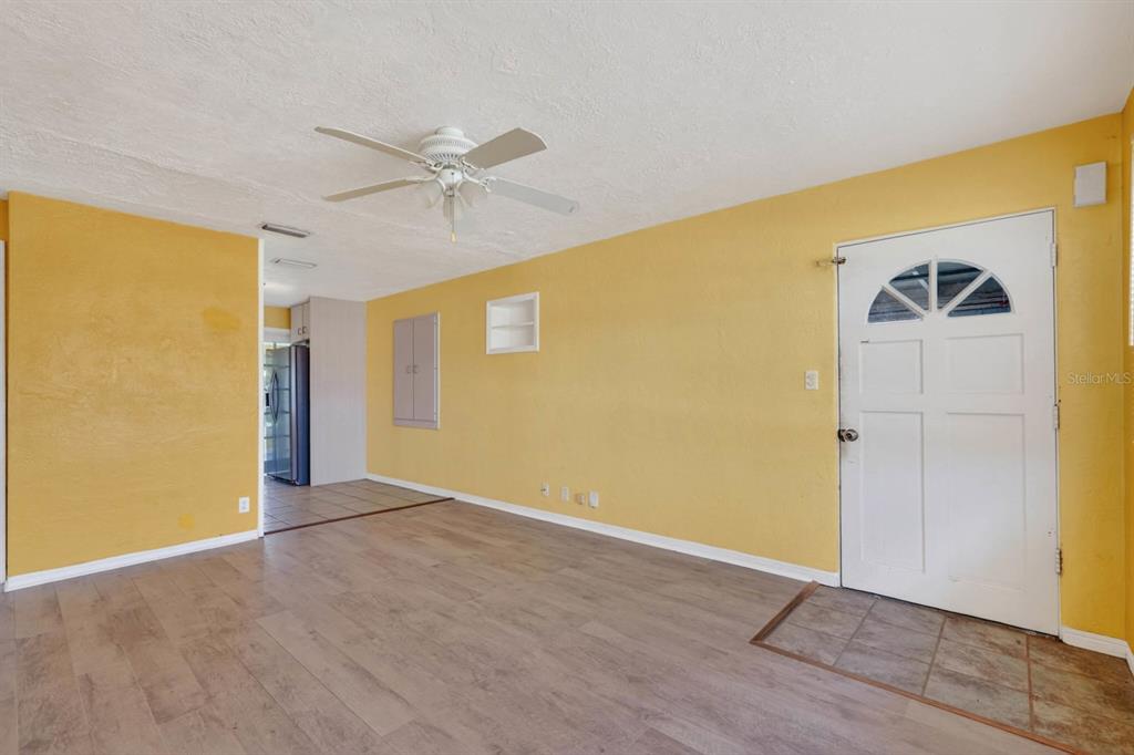 A living room with yellow walls, wood-look flooring, a ceiling fan, and a front door — 39 MARGARET ROAD, ORMOND BEACH, FL