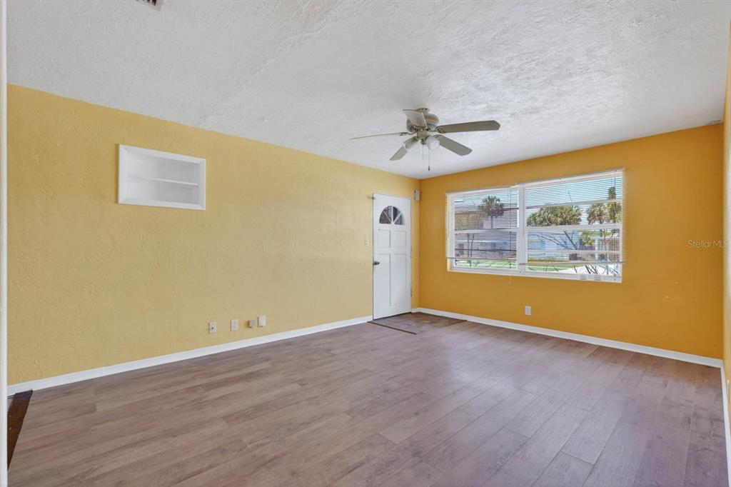 An empty living room features yellow walls, wood-look flooring, a ceiling fan, and a door — 39 MARGARET ROAD, ORMOND BEACH, FL