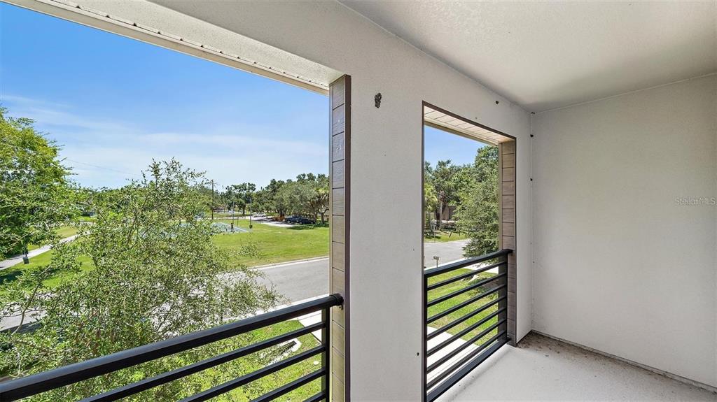 A covered balcony features white walls, dark metal railings, and a view of a park — 2587 TEMPLE STREET, SARASOTA, FL