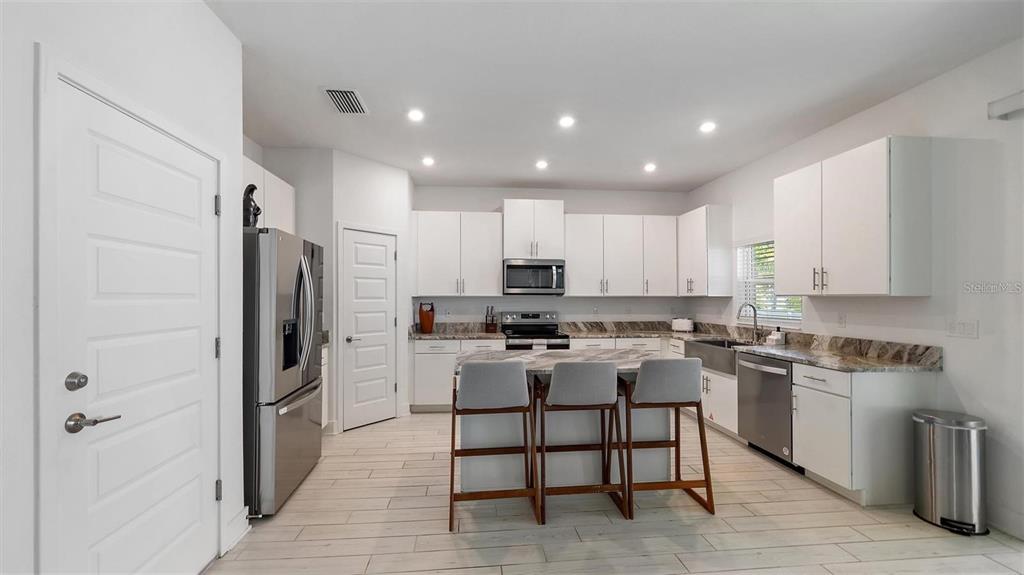 A modern kitchen features white cabinetry, stainless steel appliances, a marble-topped island, and tile flooring — 2587 TEMPLE STREET, SARASOTA, FL