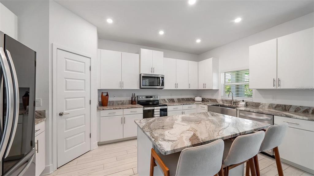 A modern kitchen features white cabinets, marble-patterned countertops, a center island, and stainless steel appliances — 2587 TEMPLE STREET, SARASOTA, FL