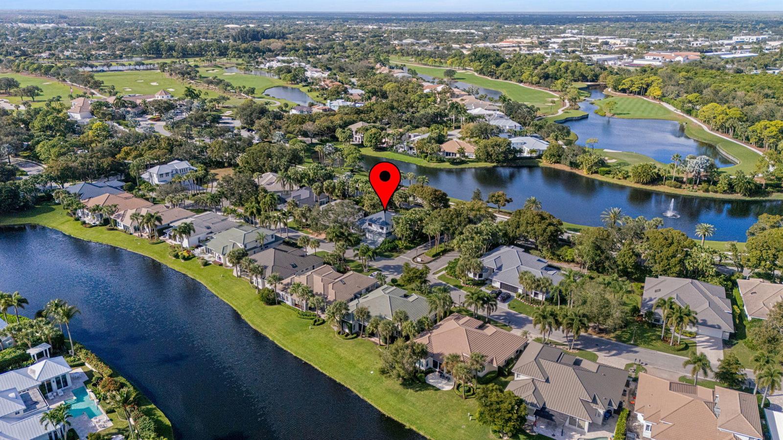 An aerial view shows a residential neighborhood with houses situated along a winding canal — 195 Birkdale Lane, Jupiter FL 33458, JUPITER, FL