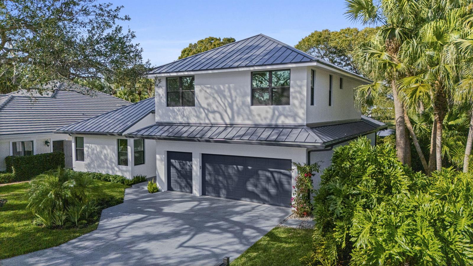 An exterior view of a two-story white house with a dark metal roof and garage — 195 Birkdale Lane, Jupiter FL 33458, JUPITER, FL