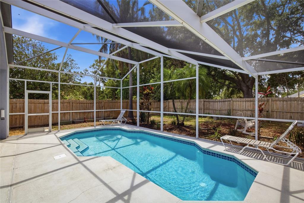 A screened-in swimming pool with a concrete deck and a wooden fence in the backyard — 7611 WILTSHIRE PARK PLACE, APOLLO BEACH, FL