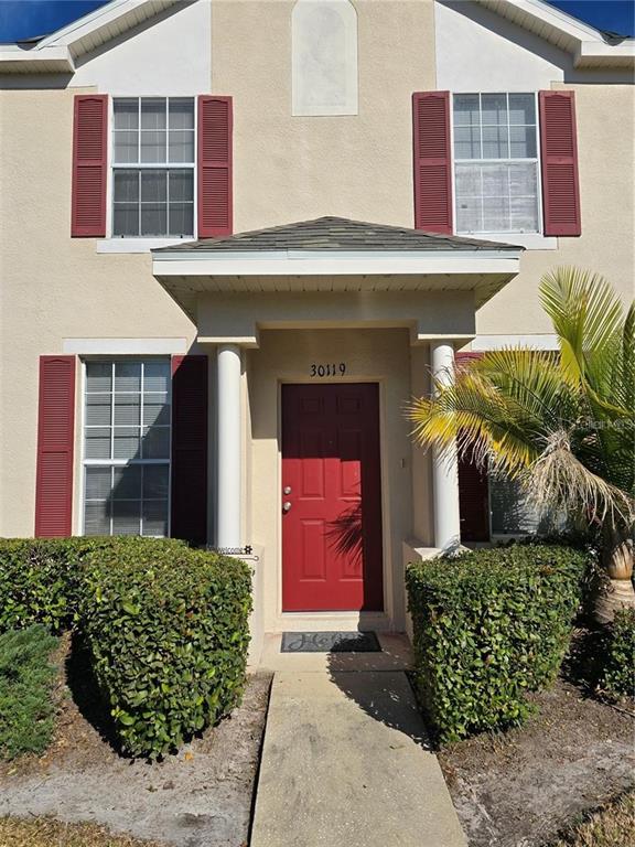 A two-story house exterior features a red front door, red shutters, and two hedges — 30119 WELLESLEY WAY, WESLEY CHAPEL, FL