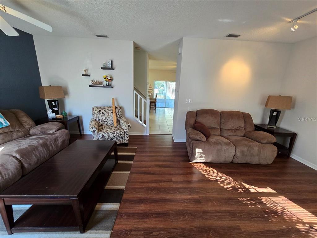A living room features brown furniture, dark wood flooring, and a view into a dining area — 30119 WELLESLEY WAY, WESLEY CHAPEL, FL