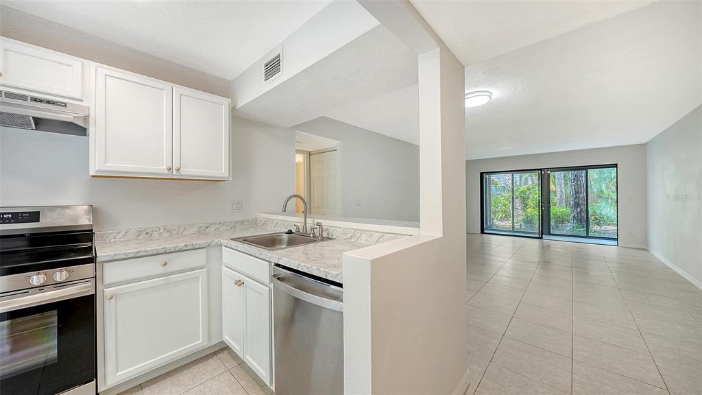 A kitchen with white cabinets and stainless steel appliances opens to a tiled living area — 1720 GLENHOUSE DRIVE UNIT 326, SARASOTA, FL
