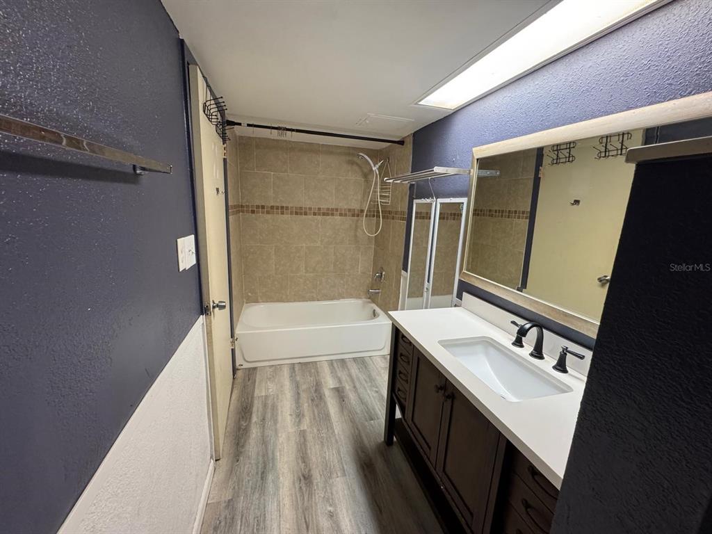 A bathroom features a dark vanity, a white sink, a tub-shower combo, and wood-look flooring — 8421 S ORANGE BLOSSOM TRAIL UNIT 420, ORLANDO, FL