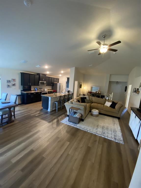 An open-concept living room and kitchen feature dark cabinetry, a large island, and wood flooring — 4634 SE 27TH STREET, OCALA, FL