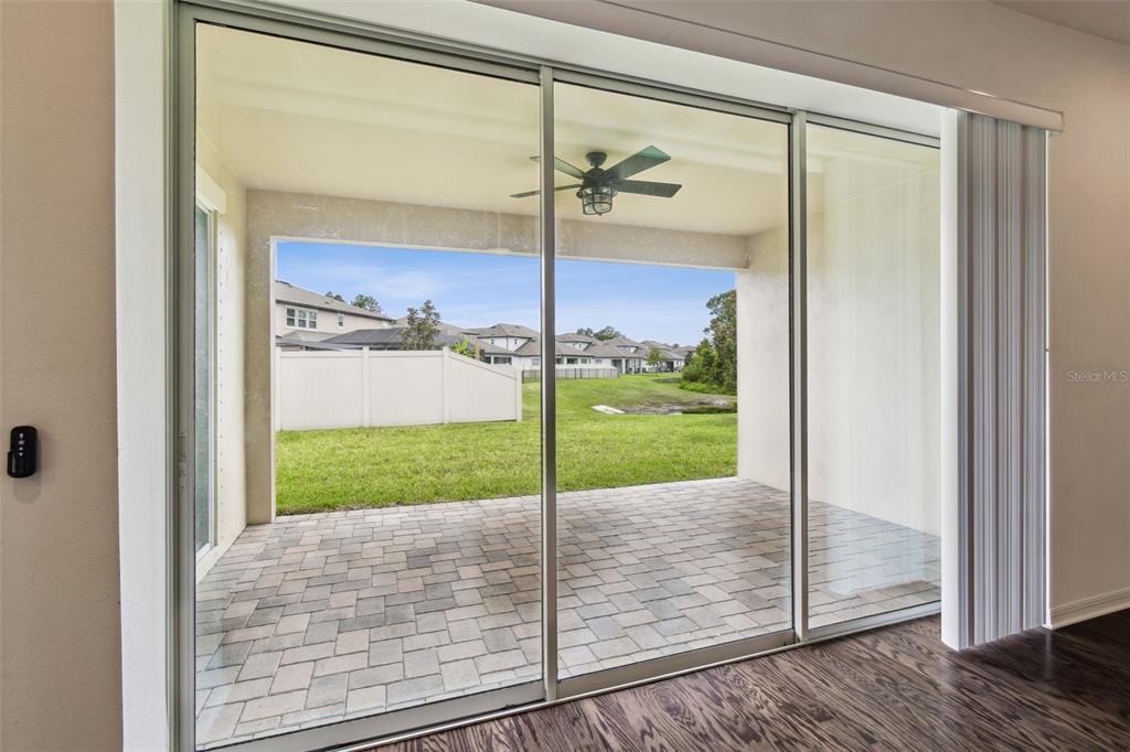 A view through sliding glass doors shows a covered patio with pavers and a backyard — 4512 TATUM LOOP, ODESSA, FL